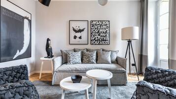 A modern living room with a grey sofa, two white side tables, a black floor lamp, and artwork on the walls.