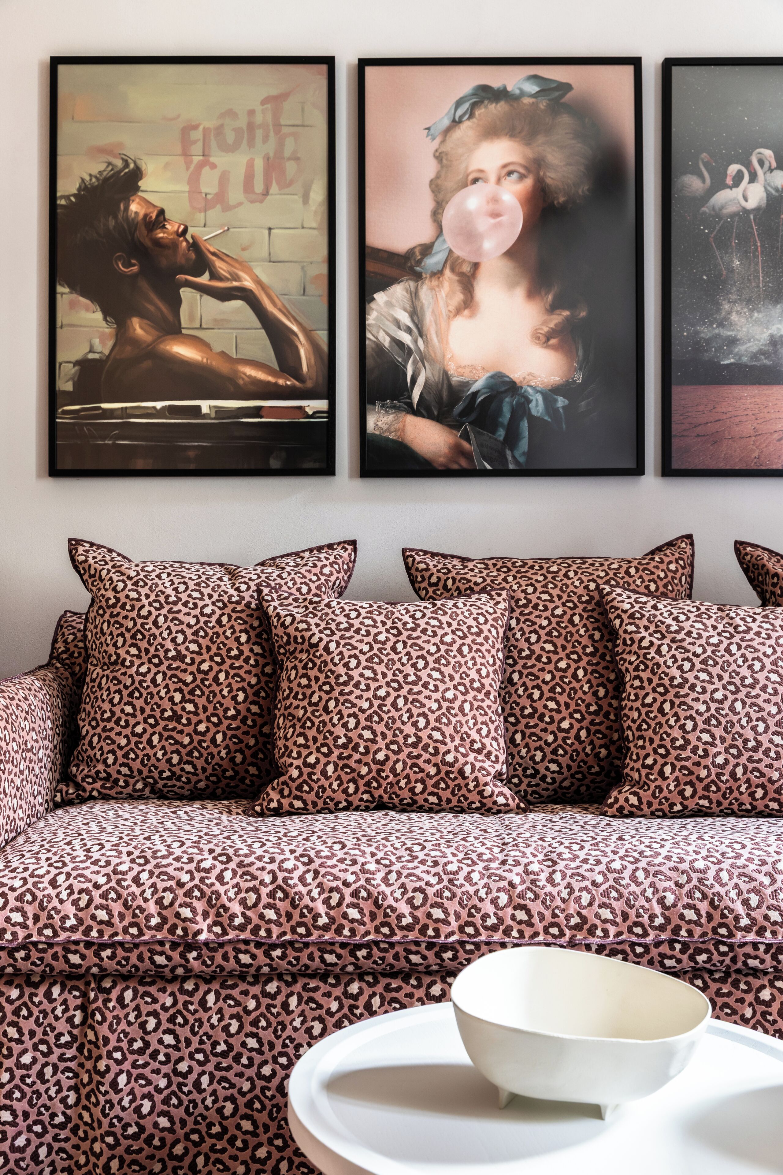 Een kamer met een bank, kussens en drie ingelijste kunstwerken aan de muur.