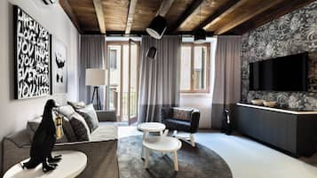 Un salon moderne avec un canapé, une table ronde, un fauteuil noir, un téléviseur et un mur décoré d’un motif.