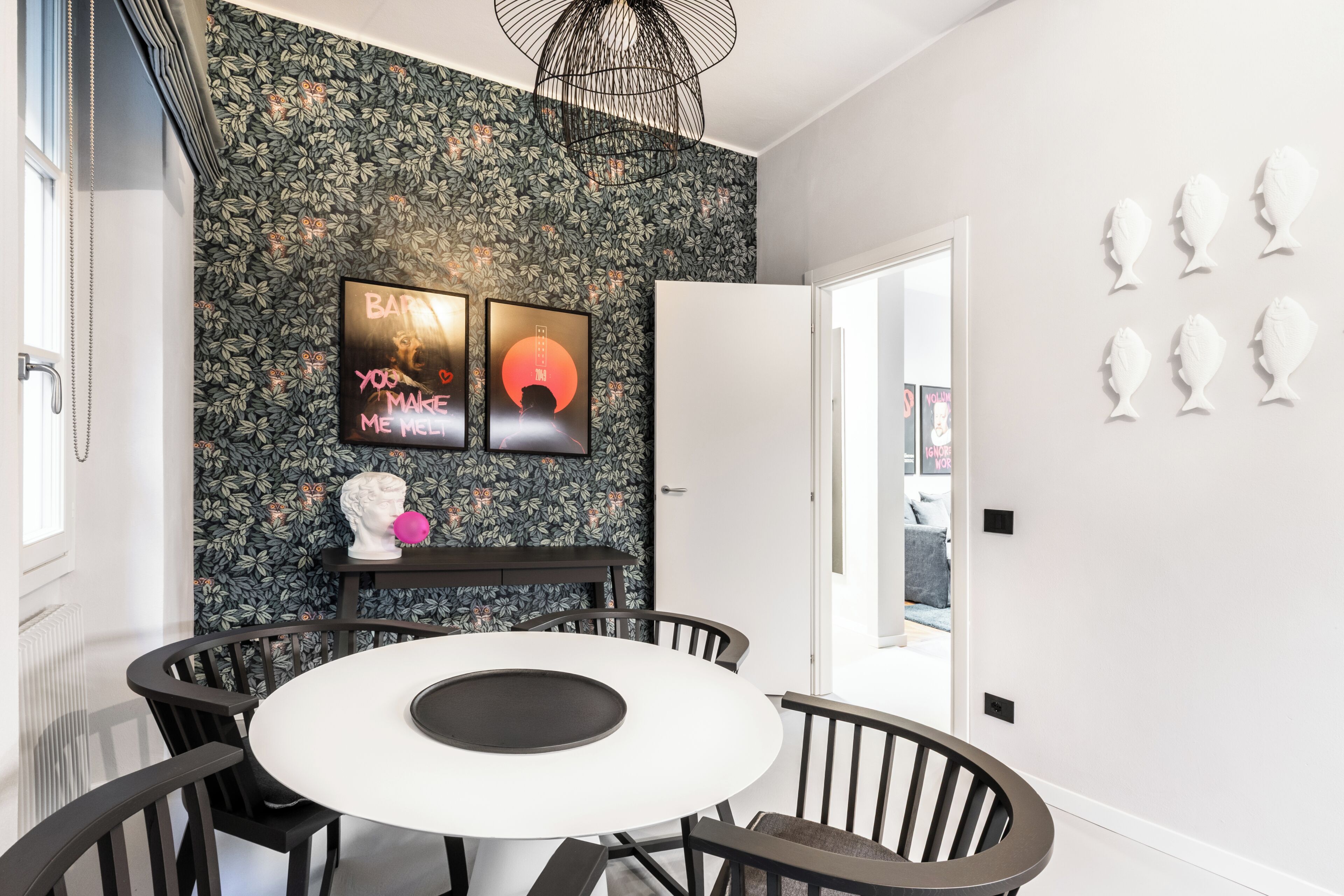 Un comedor con una mesa redonda, sillas, una pared blanco y negro con papel tapiz floral y una puerta blanca.