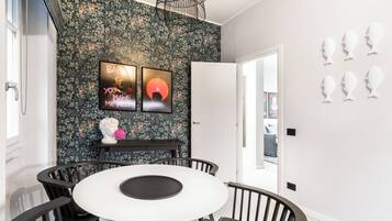 Un comedor con una mesa redonda, sillas, una pared blanco y negro con papel tapiz floral y una puerta blanca.