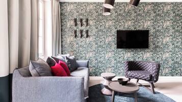 Una sala de estar moderna con un sofá gris, un sillón oscuro, una mesa de centro redonda y un televisor de pantalla plana montado en una pared con estampado floral.