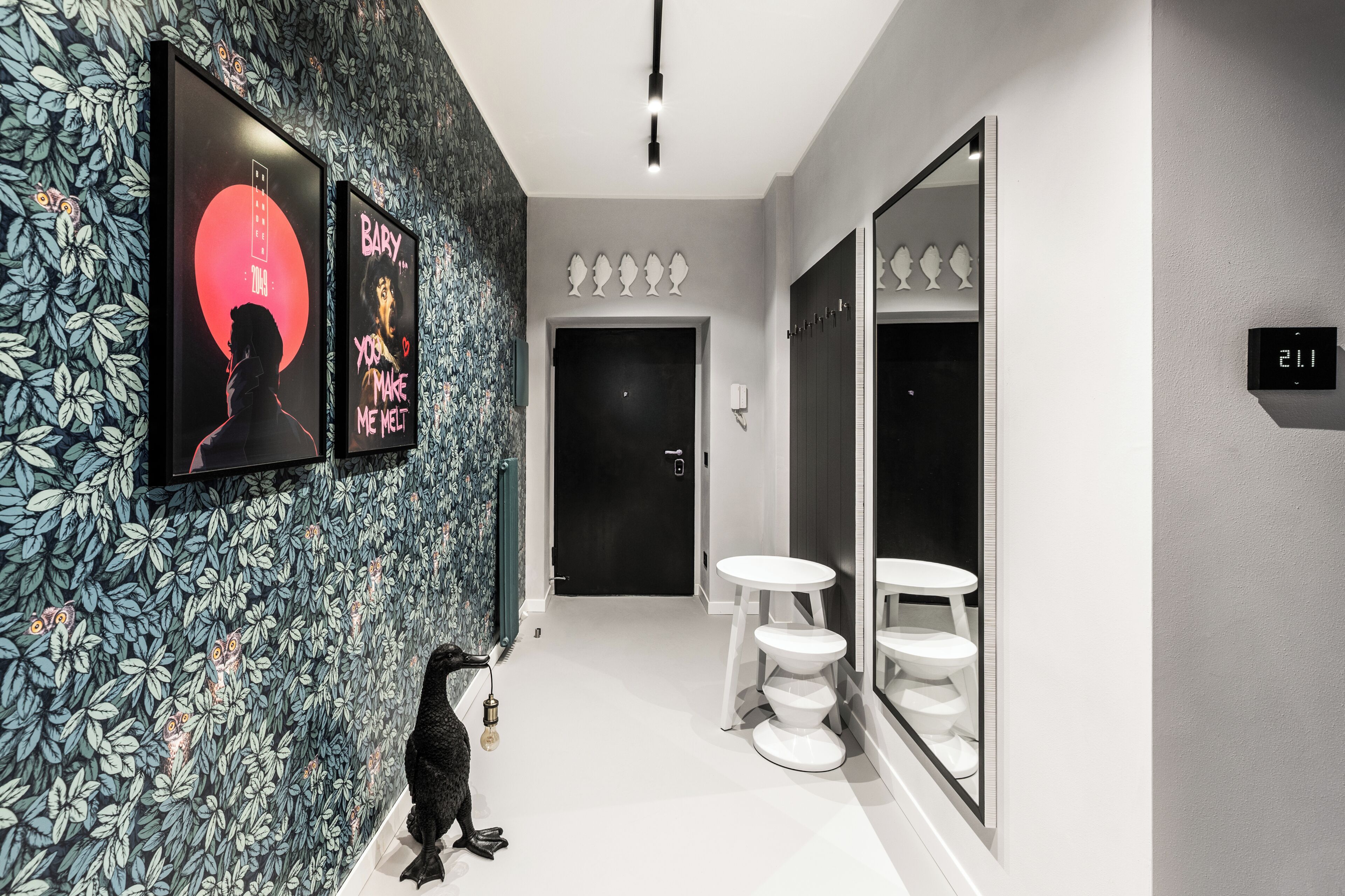 A hallway with a floral wallpaper, a black door, a white round table, and a mirror reflecting a toilet.