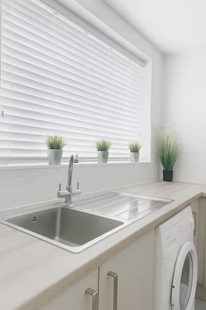Eine moderne Küche mit einer Spüle, einer eingebauten Waschmaschine und Blumentöpfen am Fensterbrett.