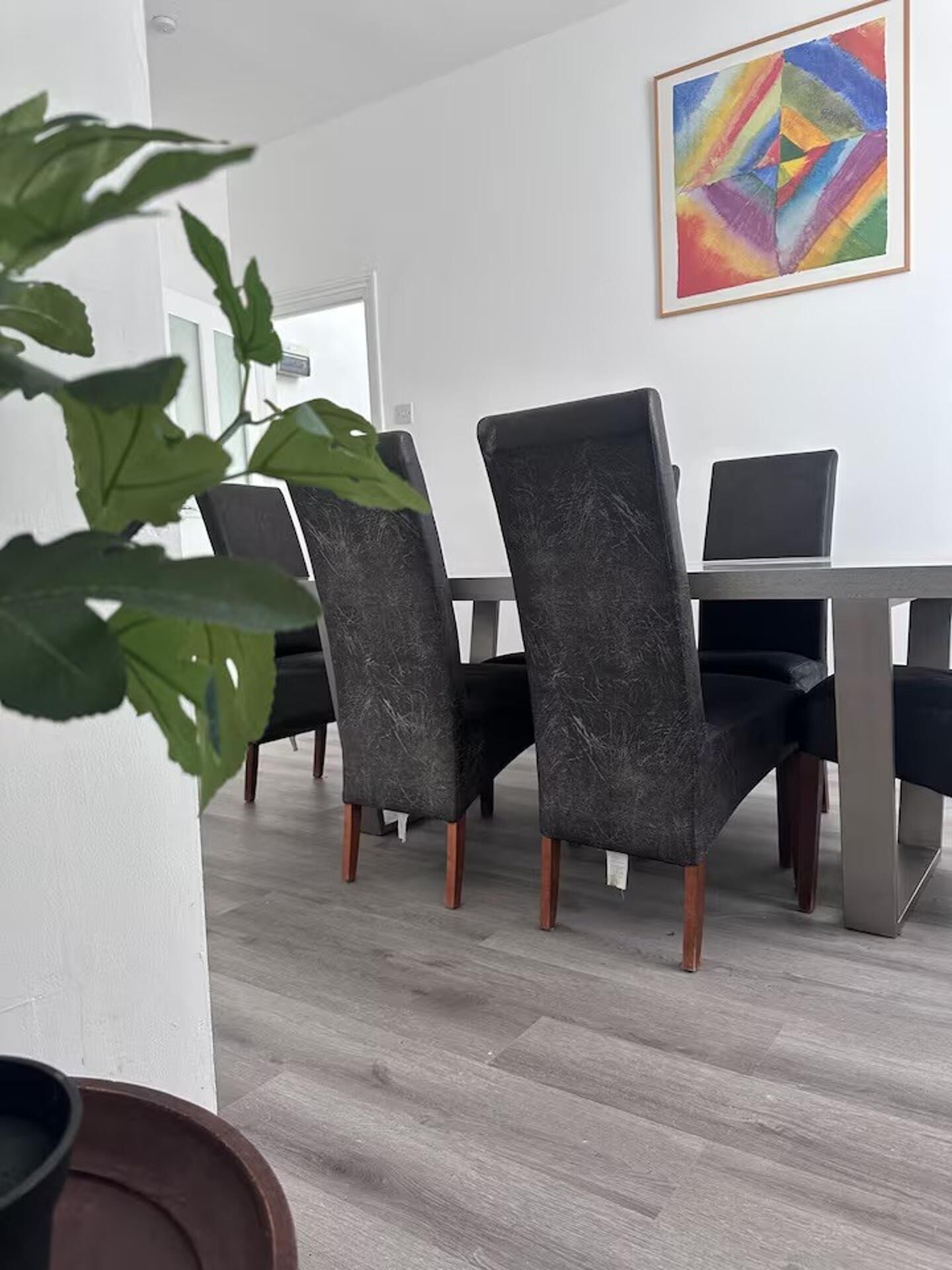 Un área de comedor moderna con una pared blanca, un cuadro abstracto colorido y una planta.