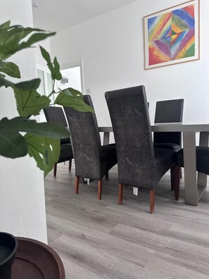 Un área de comedor moderna con una pared blanca, un cuadro abstracto colorido y una planta.