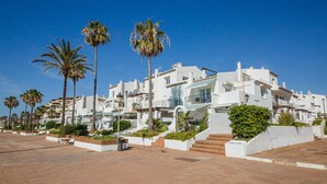 A coastal building with white facades, palm trees, and a paved walkway. - Gaviotas apartment C75 (Manilva)