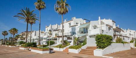 Un bâtiment situé sur la côte, avec des façades blanches, des palmiers et une promenade dallée.