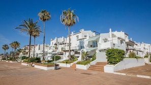 A coastal building with white facades, palm trees, and a paved walkway. - Gaviotas apartment C75 (Manilva)