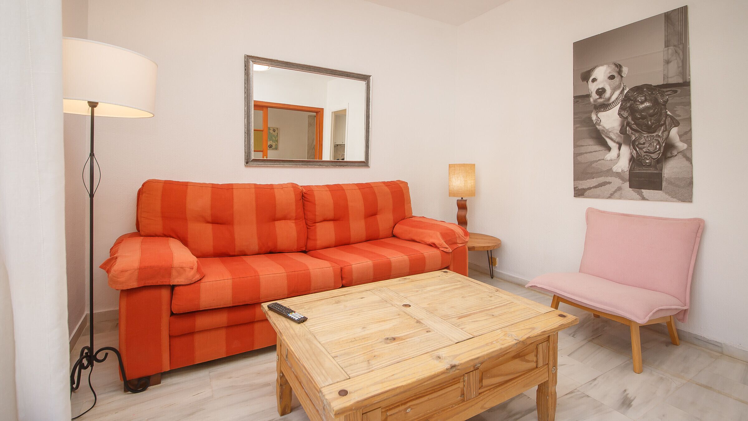Una sala de estar con un sofá, una silla, una mesa de centro, una lámpara y un espejo.