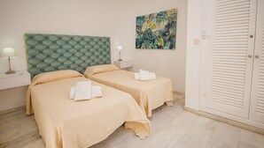 A hotel room with two beds, a green tufted headboard, a painting, a bedside table with a lamp, and a white door. - Gaviotas apartment C75 (Manilva)