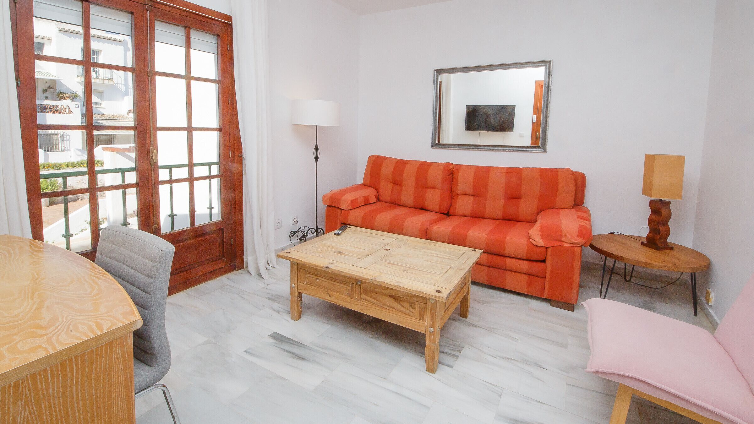 Una sala de estar con un sofá, una mesa de centro, una silla, una lámpara y un televisor.