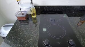 Een keuken met een zwart elektrische fornuis, een wit stopcontact en een fles olie op het aanrecht.