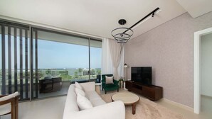 Un salon moderne doté d’un grand canapé, d’un téléviseur et offrant une vue sur l’extérieur grâce à de grandes fenêtres du sol au plafond.