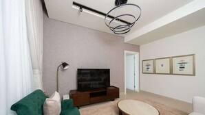 Un salon moderne avec un téléviseur à écran plat, un canapé vert, une table basse ronde et des œuvres d’art encadrées accrochées au mur.