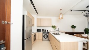 Une cuisine moderne dotée d’un réfrigérateur en acier inoxydable, d’un lave-linge encastré et d’un plan de travail blanc.