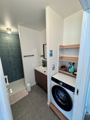 Ein kleines Badezimmer mit Dusche, Toilette, Waschbecken und einer Waschmaschine mit Frontlader.