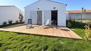 Un edificio blanco con terraza de madera, dos sillas y una parrilla.
