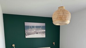 Un dormitorio con una cama blanca, una pared verde, un cuadro de un paisaje nevado y una lámpara de fibra trenzada.
