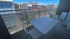 Un balcón con una mesa y sillas, barandilla metálica y vistas a edificios.