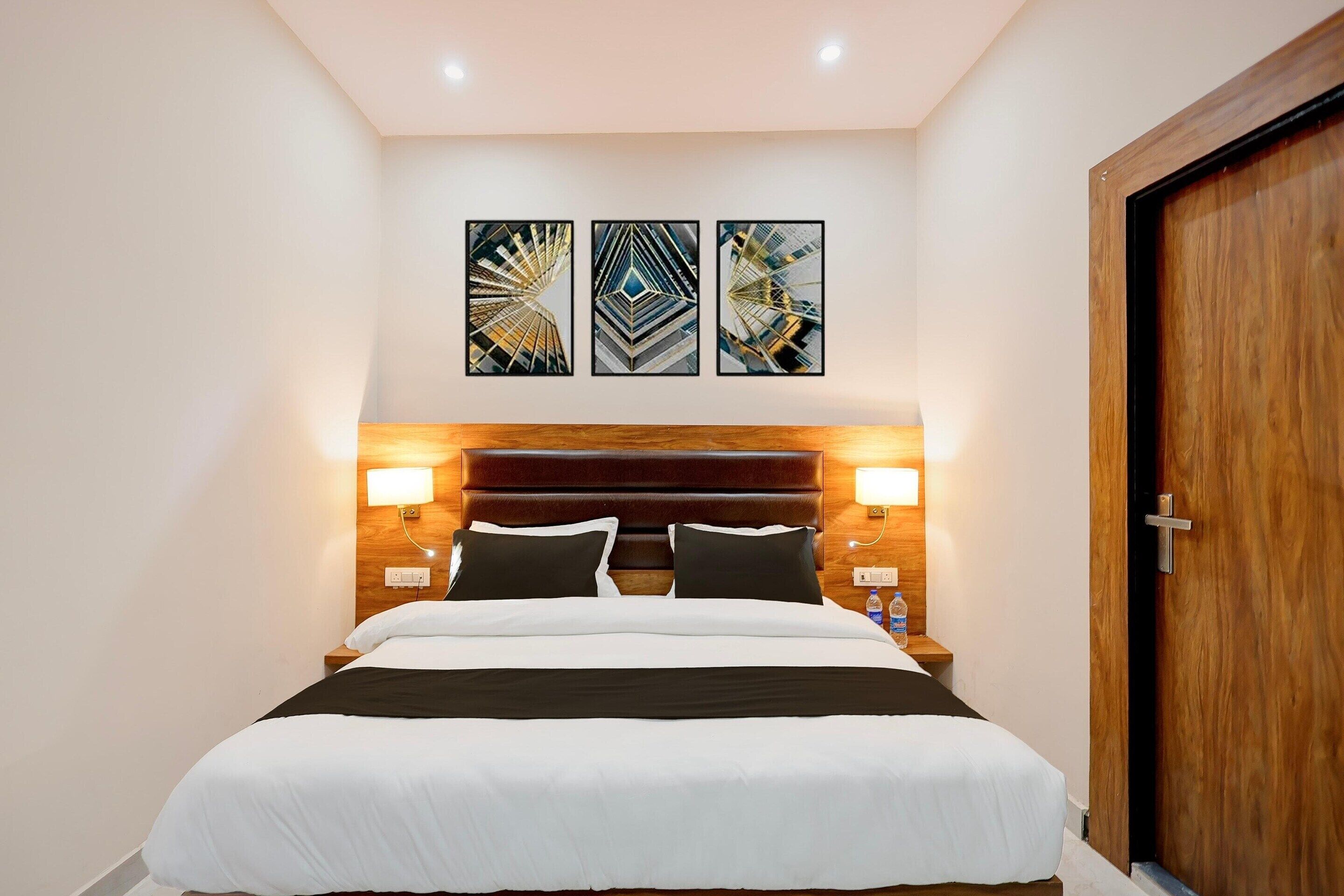 Una camera d'albergo con un letto, due lampade a parete e una porta in legno.
