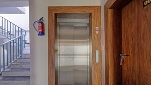 An elevator with a fire extinguisher mounted on the wall, a no-smoking sign, and a wooden door frame. - Premium Valley View With Balcony Haldwani (Haldwani)