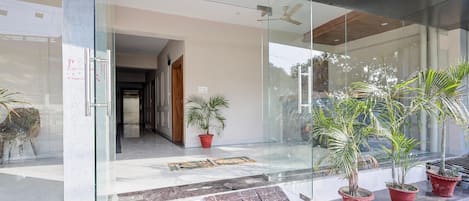 Entrada de un edificio moderno con puertas de vidrio, un banco de madera y plantas en macetas.