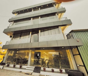 Um edifício de vários andares com design arquitetônico moderno, com entrada de vidro e vasos de plantas na base.