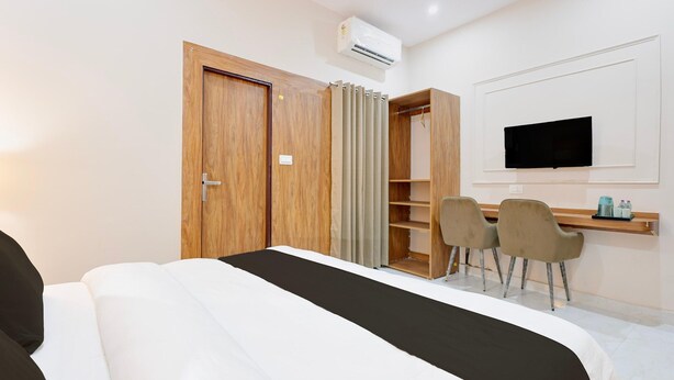 A hotel room with a bed, a desk with chairs, a television, and a wardrobe. - Premium Valley View With Balcony Haldwani (Haldwani)