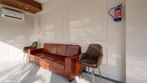 A modern room with a brown leather sofa, two chairs, a wall-mounted fire extinguisher, and an air conditioning unit. - Premium Valley View With Balcony Haldwani (Haldwani)
