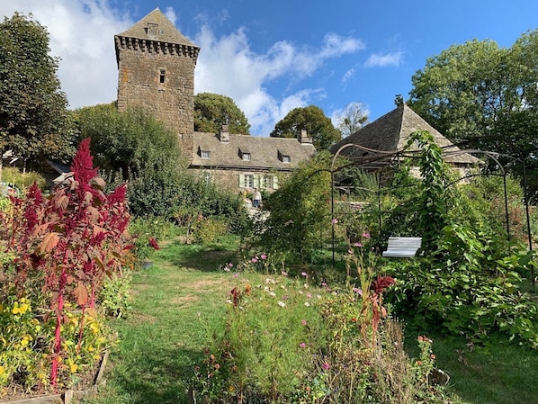 A historic stone building with a tower, surrounded by a garden with various plants and flowers.