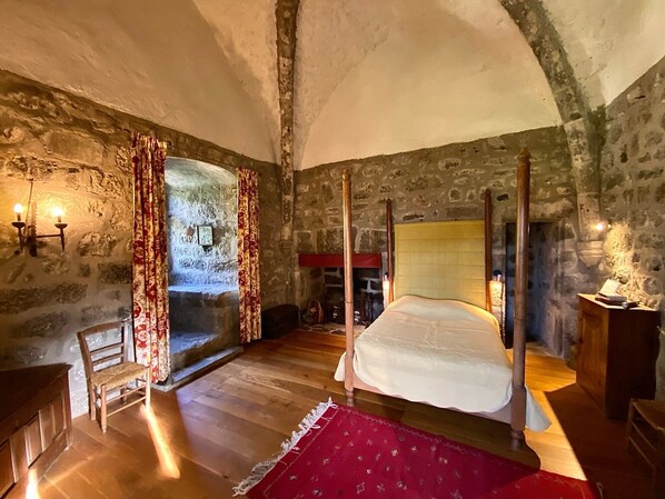 Une chambre aux murs de pierre, dotée d’un lit à baldaquin, d’un plancher en bois et d’un tapis rouge à motifs.