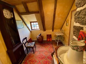 Um quarto rústico com teto de madeira, um relógio, uma cadeira, uma mesa e um tapete.