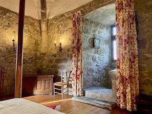 A stone-walled room with a wooden chair, a bed, and a stone bench.