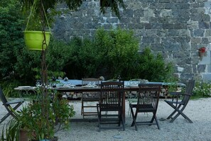 Un espace de restauration en plein air avec un mur en pierre en arrière-plan, un pot de fleurs suspendu et un sol recouvert de gravier.