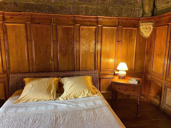 Une pièce avec un lit en bois, une table de chevet avec une lampe et un mur en pierre.
