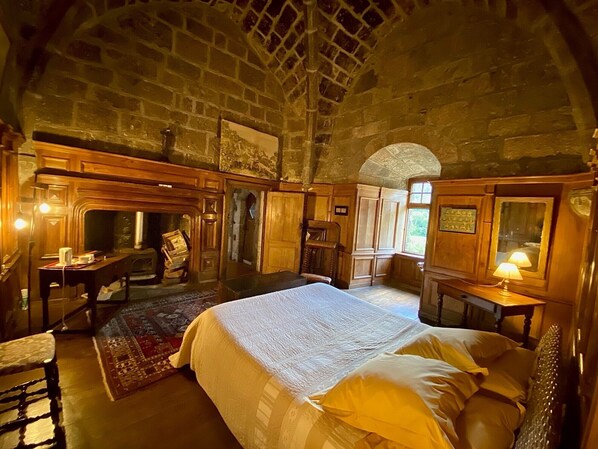 A room with a bed, wooden furniture, a desk, and a stone wall.