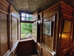 En hall med träpanel på väggarna, ett fönster som vetter ut mot en trädgård och en inramad tavla på väggen.