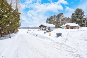A snow-covered road with a wooden structure and a small building with a snow-covered roof. - Spa & Nature Retreat - Le Bercail (Entrelacs)