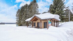 A wooden cabin with a snow-covered roof, a bench, and a sign indicating it's a place for overnight stays. - Spa & Nature Retreat - Le Bercail (Entrelacs)