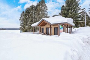 A wooden cabin with a snow-covered roof, a bench, and a sign indicating it's a place for overnight stays. - Spa & Nature Retreat - Le Bercail (Entrelacs)