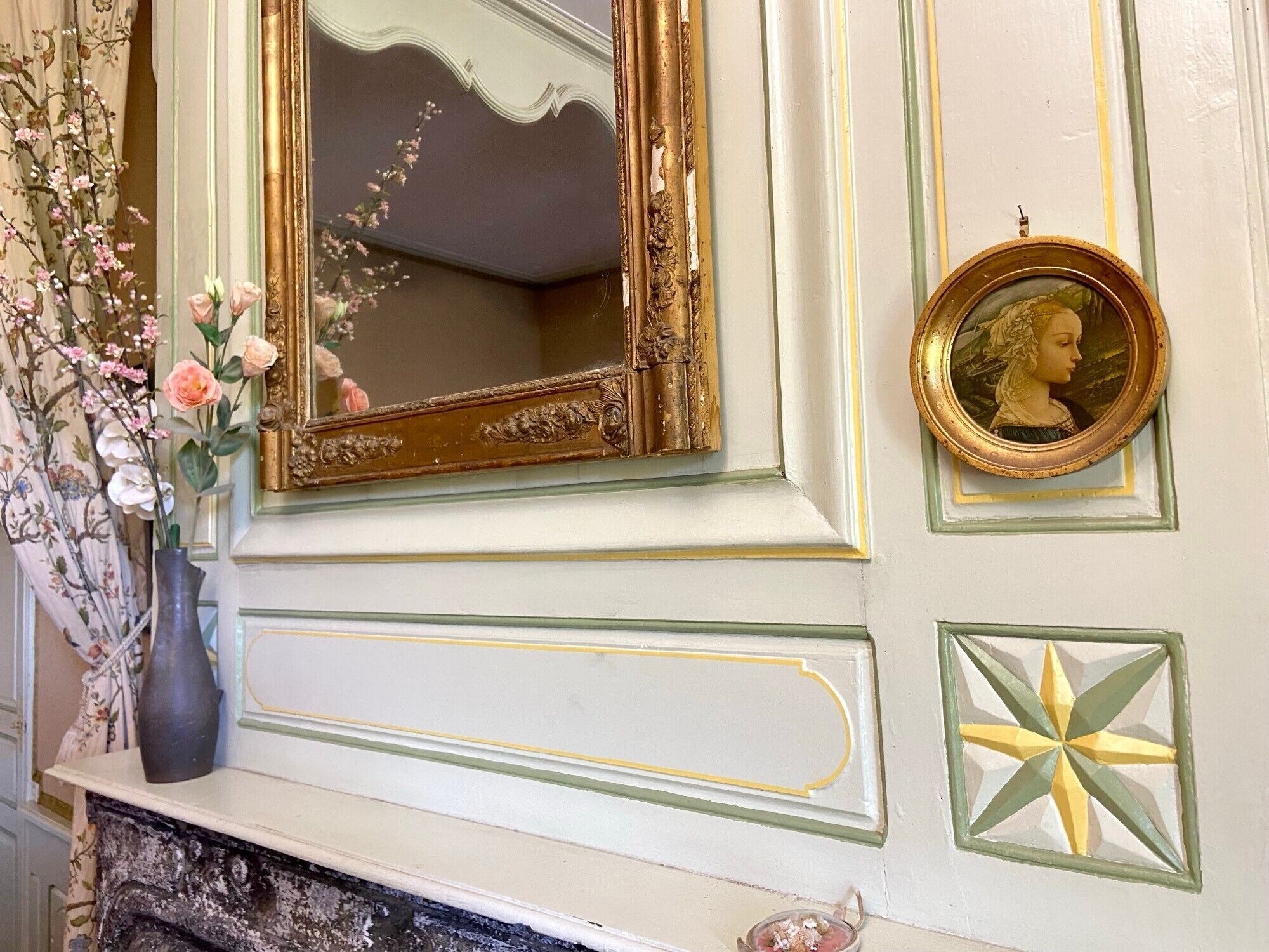 A wall with a mirror, a framed portrait, and a decorative star pattern.