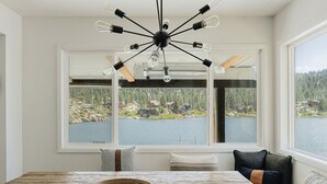 Ein Zimmer mit Esstisch, einem besonderen Kronleuchter und großen Fenstern mit Blick auf See und Wald.