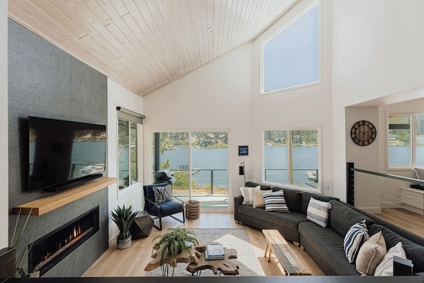 Ein geräumiges Wohnzimmer mit Kamin, Fernseher und großem Fenster mit Seeblick.
