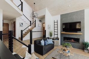 Ein modernes Wohnzimmer mit Treppe, Flachbildfernseher, Kamin und einer großen Pflanze.