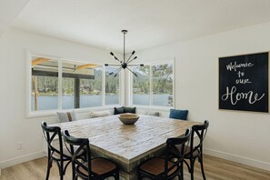 A dining area with a wooden table, black chairs, a bowl, a ceiling fan, and a window with a view of a lake.