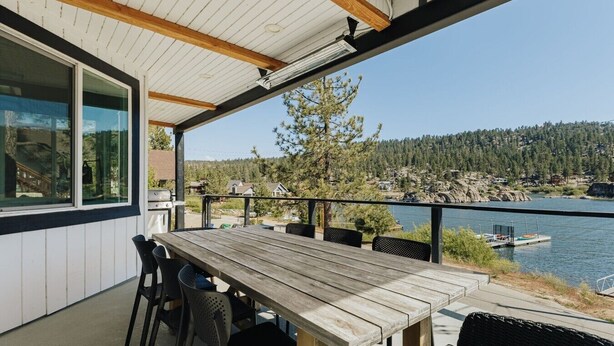 Eine Holterrasse mit Tisch und Stühlen, mit Blick auf einen See, im Hintergrund Boote und Häuser.