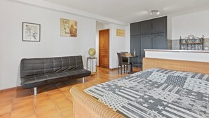 A modern living room with a sofa, a bed with a patterned bedspread, a dining table with chairs, and a kitchen area with cabinets. - Villa Esperanza – Air-Conditioned Studio with Sea View Terrace (Cavalaire-sur-Mer)