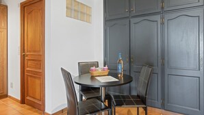 A room with a wooden door, a dark grey wardrobe, a round table with chairs, and a bottle on the table. - Villa Esperanza – Air-Conditioned Studio with Sea View Terrace (Cavalaire-sur-Mer)