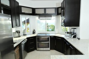 Cozinha moderna com armários pretos, eletrodomésticos de aço inoxidável e uma grande janela com vista para o exterior.